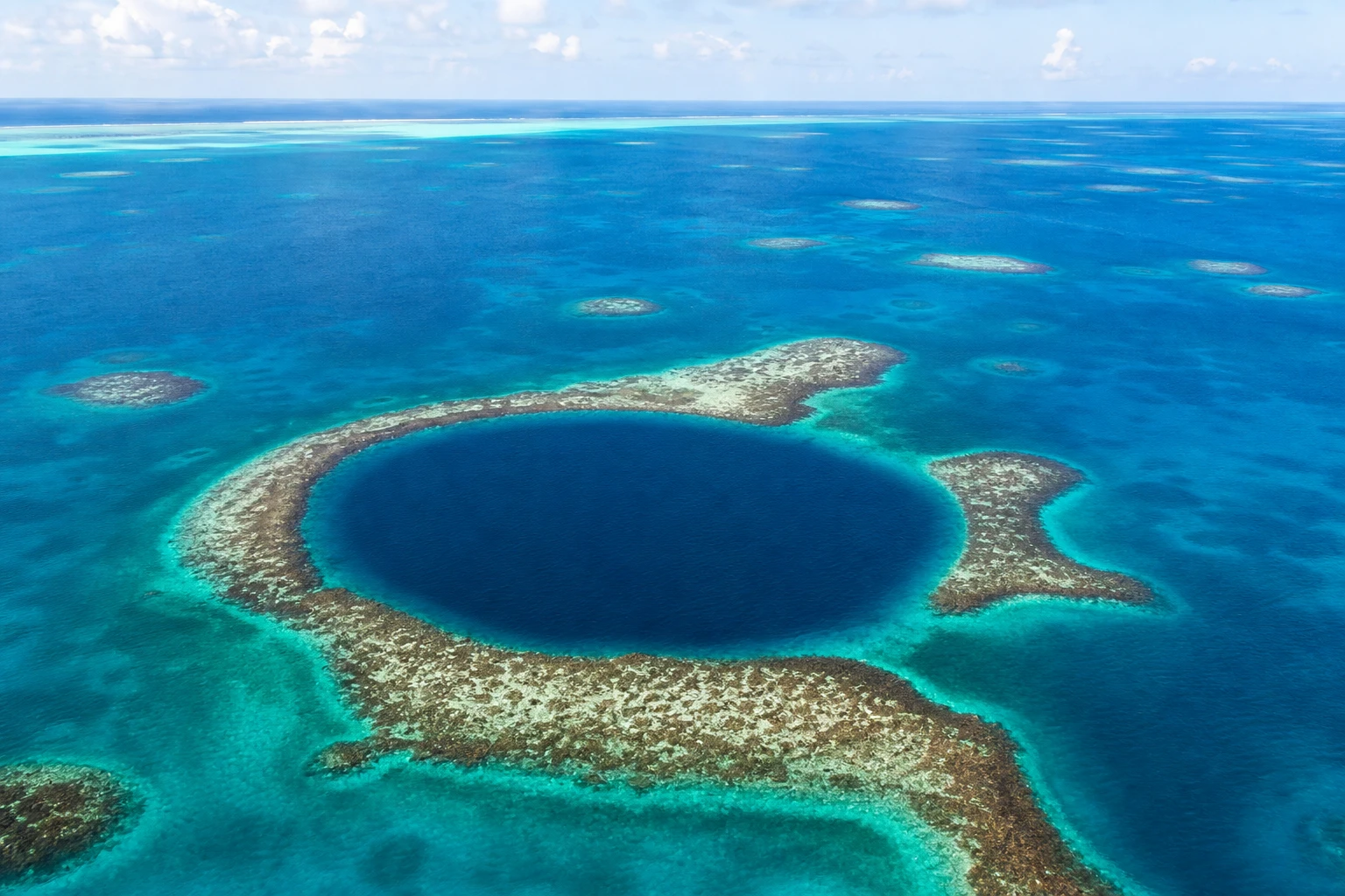 Aerial view of the Great Blue Hole surrounded by turquoise reef water in Belize
